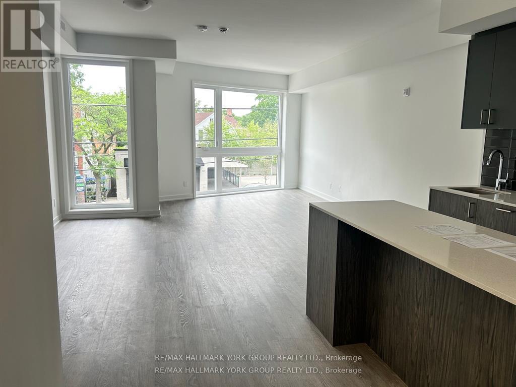 A spacious, empty room with a kitchen area and a view of the outdoors through the windows.