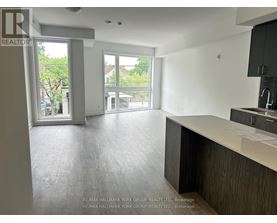 A spacious, empty room with a kitchen area and a view of the outdoors through the windows.