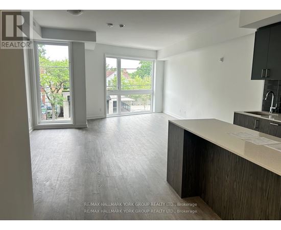 A spacious, empty room with a kitchen area and a view of the outdoors through the windows.