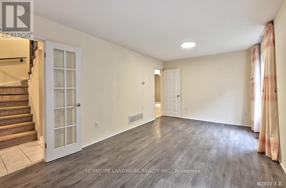A spacious room with wooden flooring and a staircase on the left side.