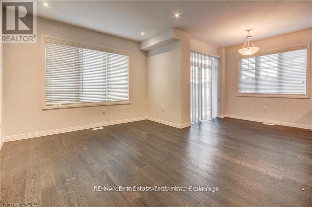 A spacious room with wooden flooring and two windows with blinds.
