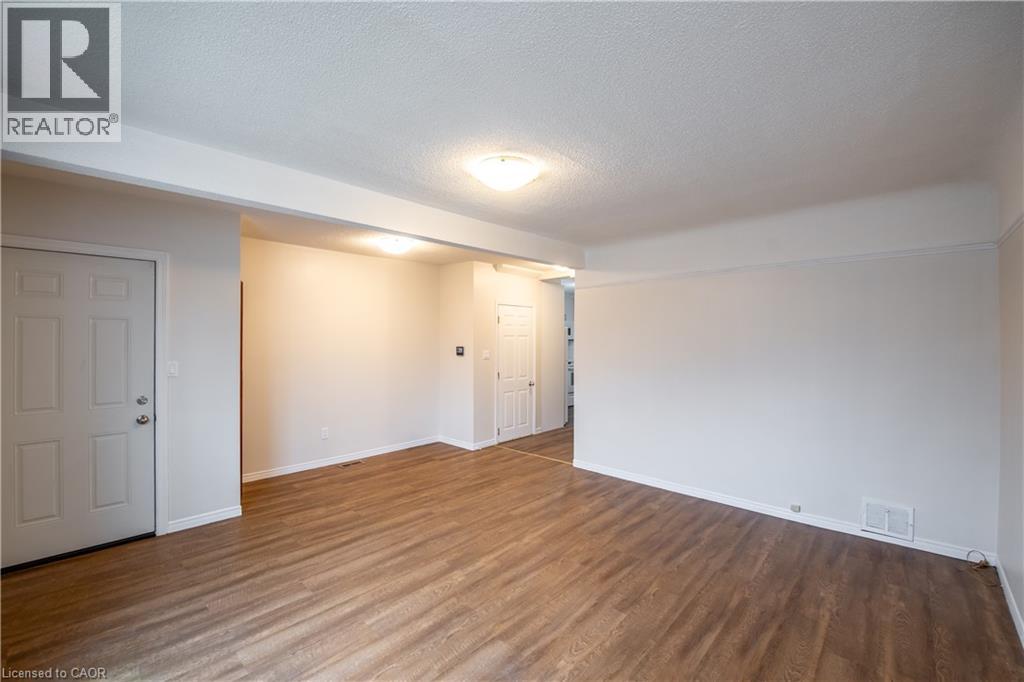 A room with wooden floors and white walls, with a door on the left and a window on the right.