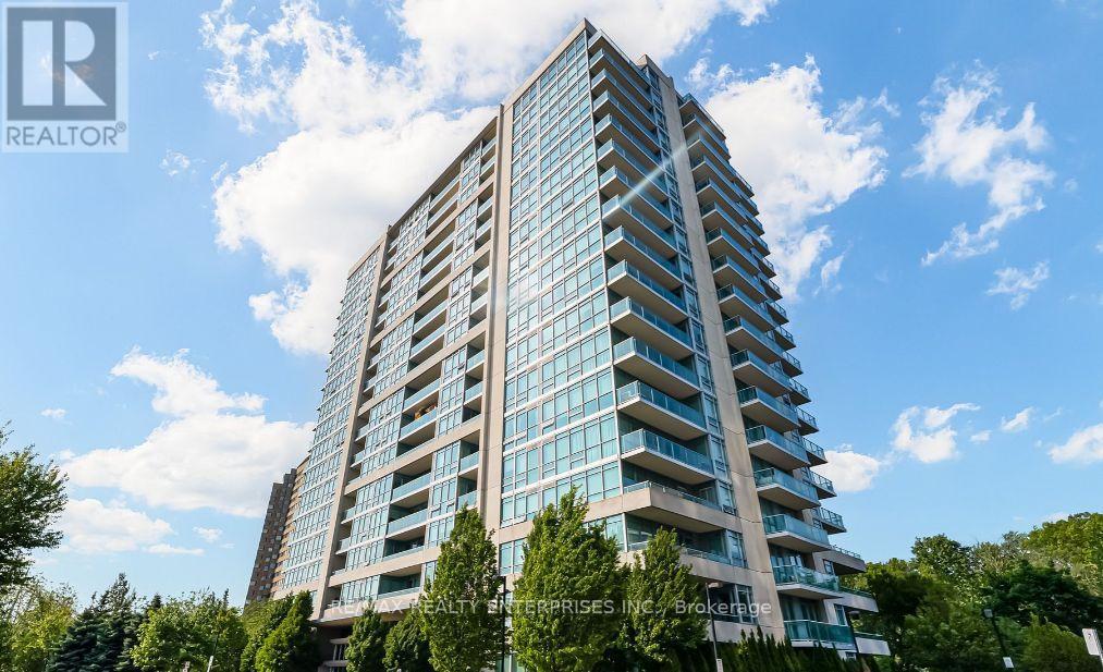 A tall residential building with a glass facade stands under a blue sky with clouds.