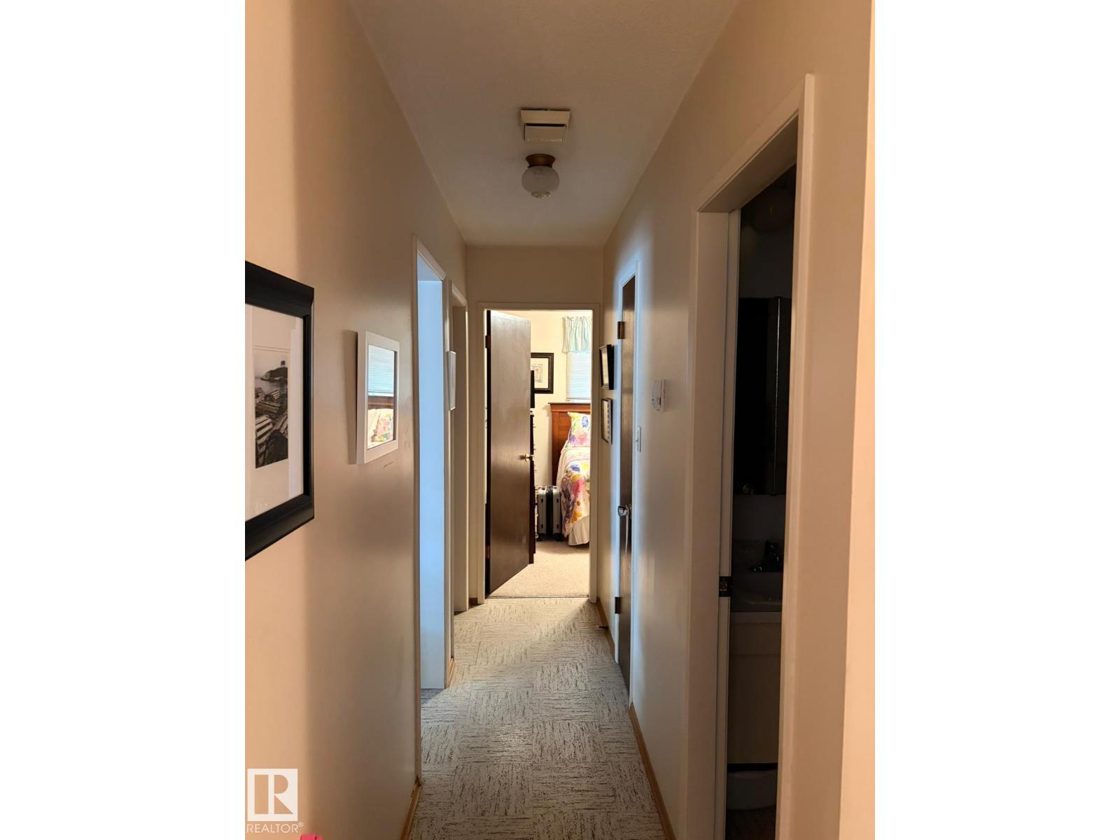 A hallway with a carpeted floor and framed pictures on the wall.