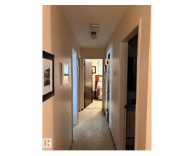 A hallway with a carpeted floor and framed pictures on the wall.
