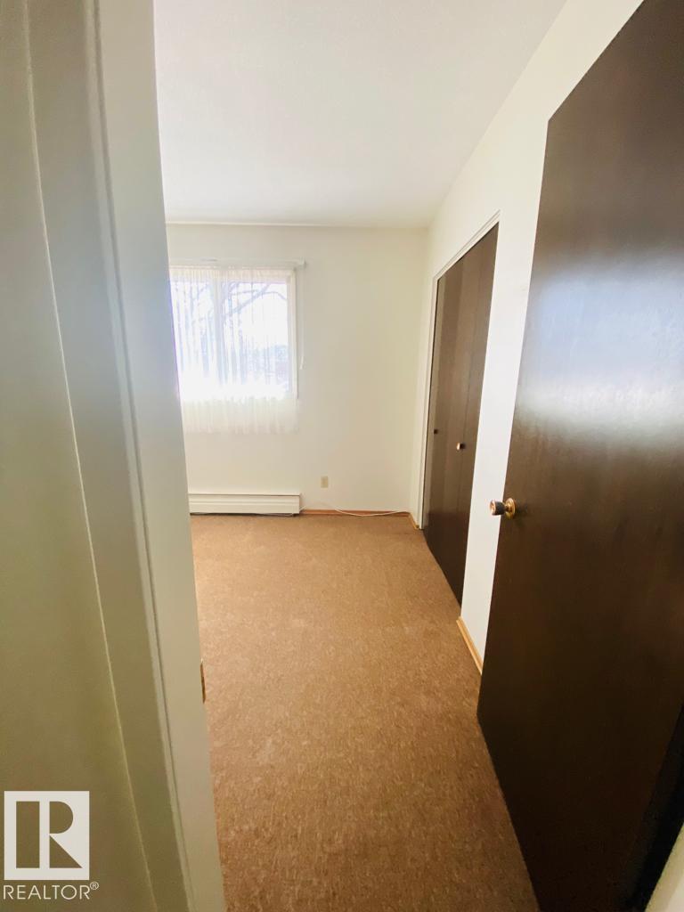 A hallway with a brown carpet and a window with blinds.