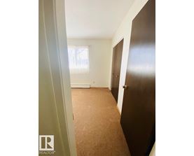 A hallway with a brown carpet and a window with blinds.