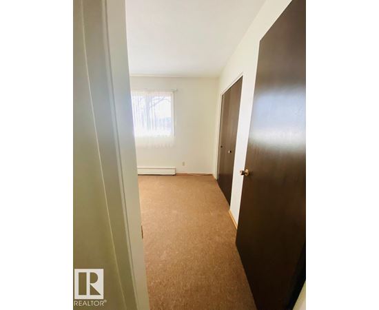 A hallway with a brown carpet and a window with blinds.