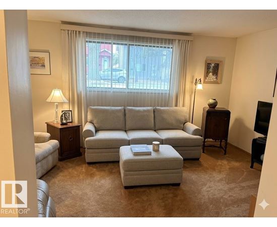 A living room with a grey sofa, a small table with a lamp and a picture frame, and a window with curtains.