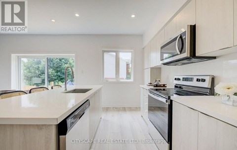 A modern kitchen with white cabinets and appliances, a microwave above the stove, and a dining area with chairs and a table.