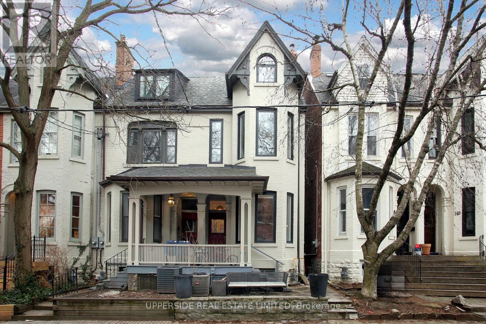 A large white house with a porch and a tree in front.