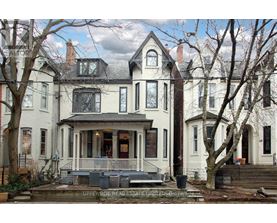 A large white house with a porch and a tree in front.