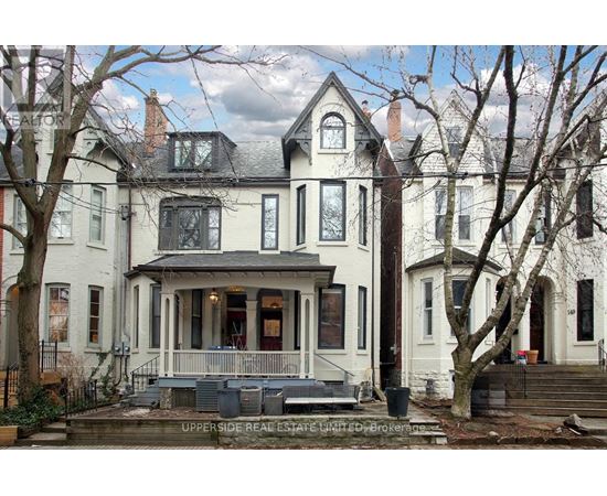 A large white house with a porch and a tree in front.