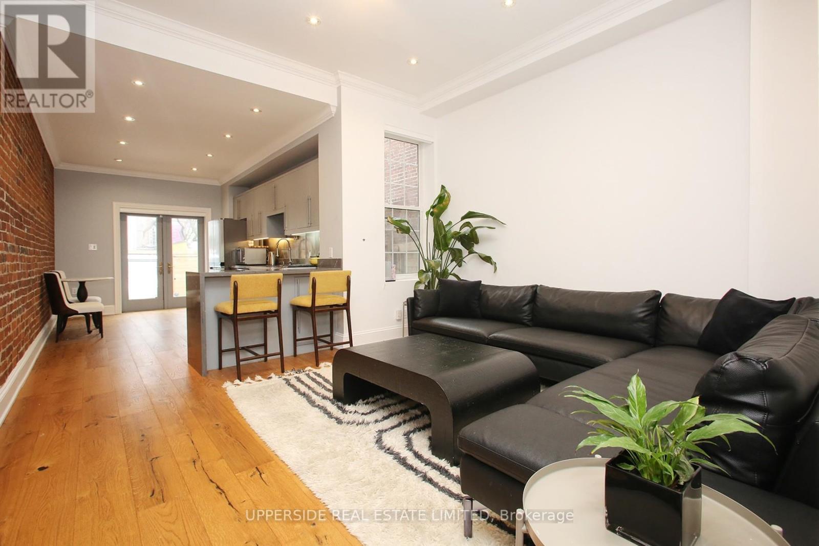 A living room with a black leather couch and a wooden floor.