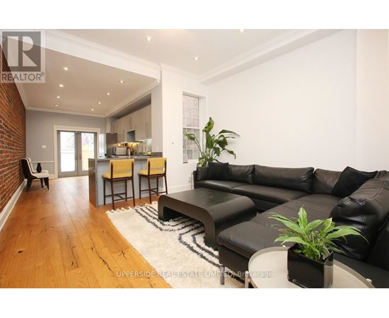 A living room with a black leather couch and a wooden floor.