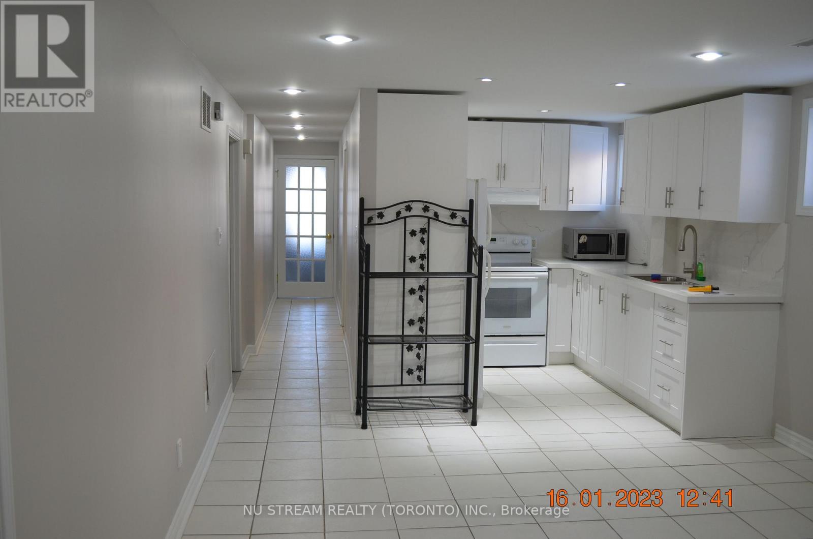 A white kitchen with a black fridge and a white tiled floor.