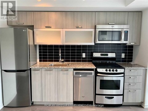 A kitchen with a stainless steel refrigerator, a microwave above the stove, and a black and white tiled backsplash.
