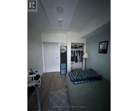 A bedroom with a bed, a nightstand with a lamp, and a closet with clothes.