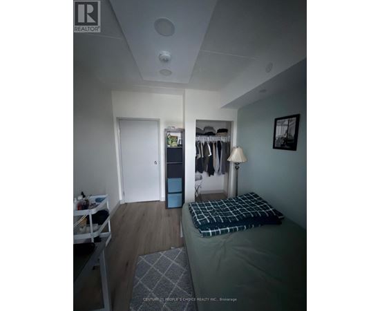 A bedroom with a bed, a nightstand with a lamp, and a closet with clothes.