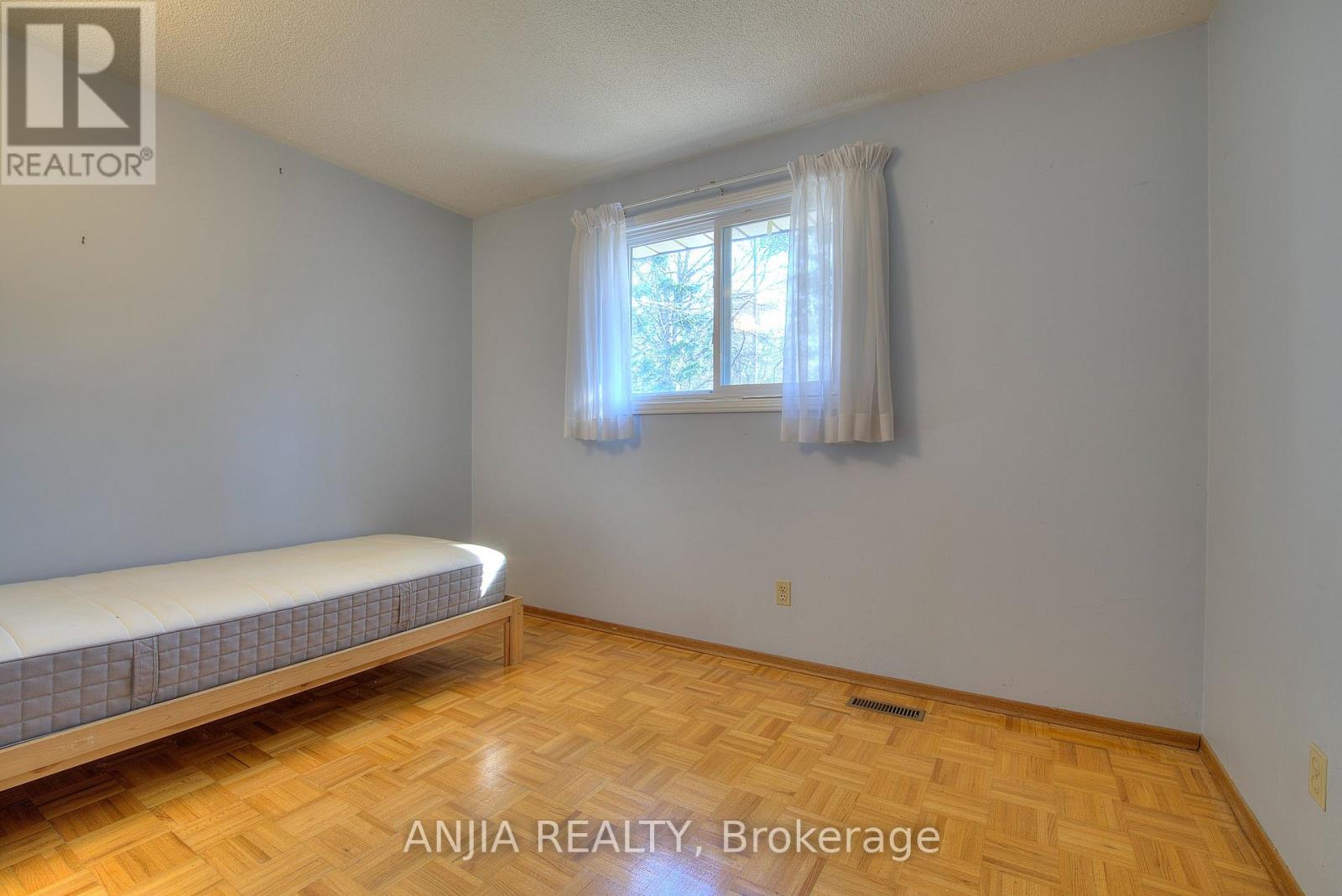 A bedroom with a bed, wooden floor, and a window with white curtains.
