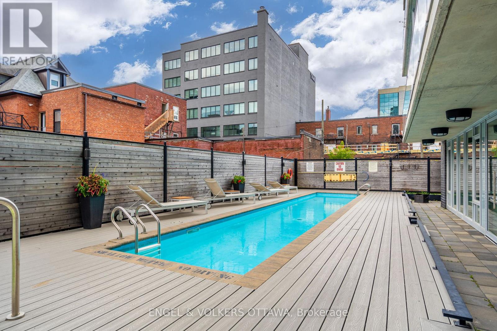 A pool surrounded by a wooden deck in an urban setting.