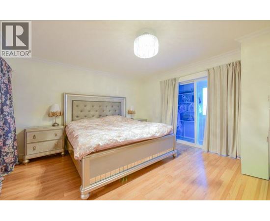A bedroom with a large bed, a nightstand, and a window with curtains.