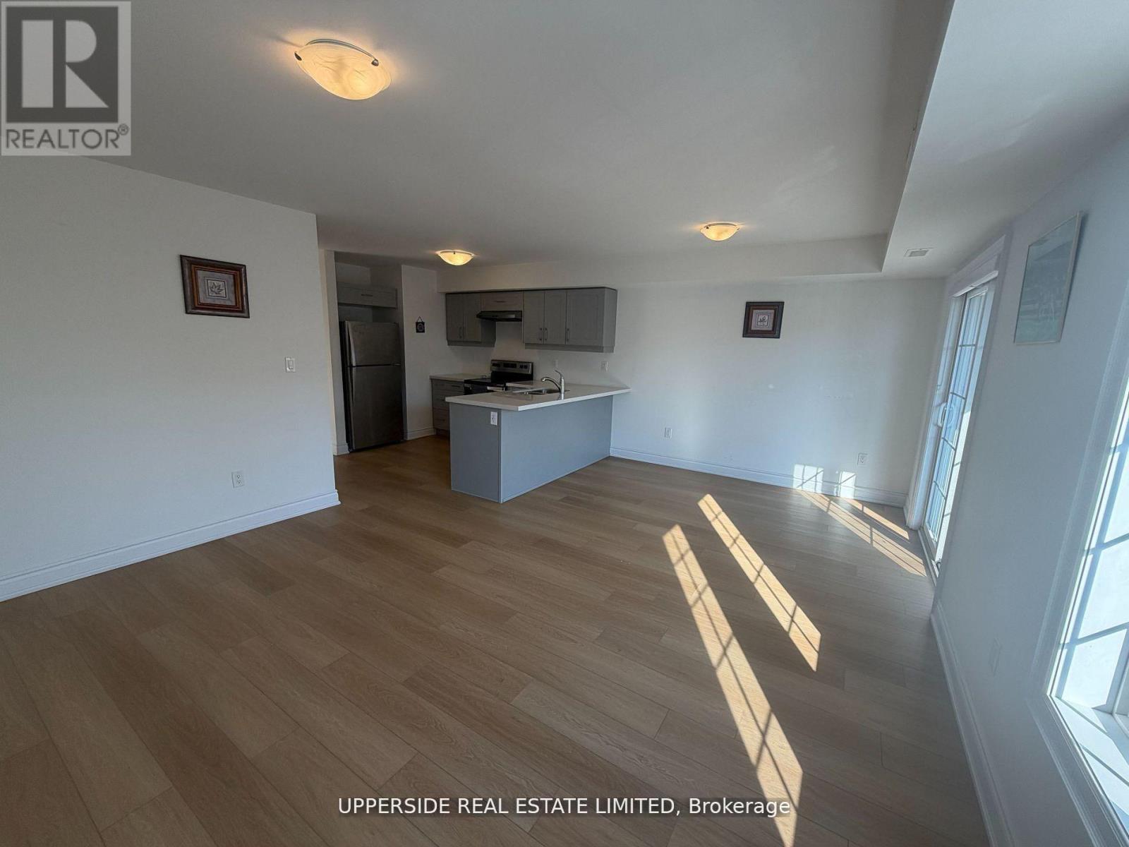 A spacious room with wooden flooring and a kitchen area in the background.