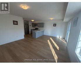 A spacious room with wooden flooring and a kitchen area in the background.