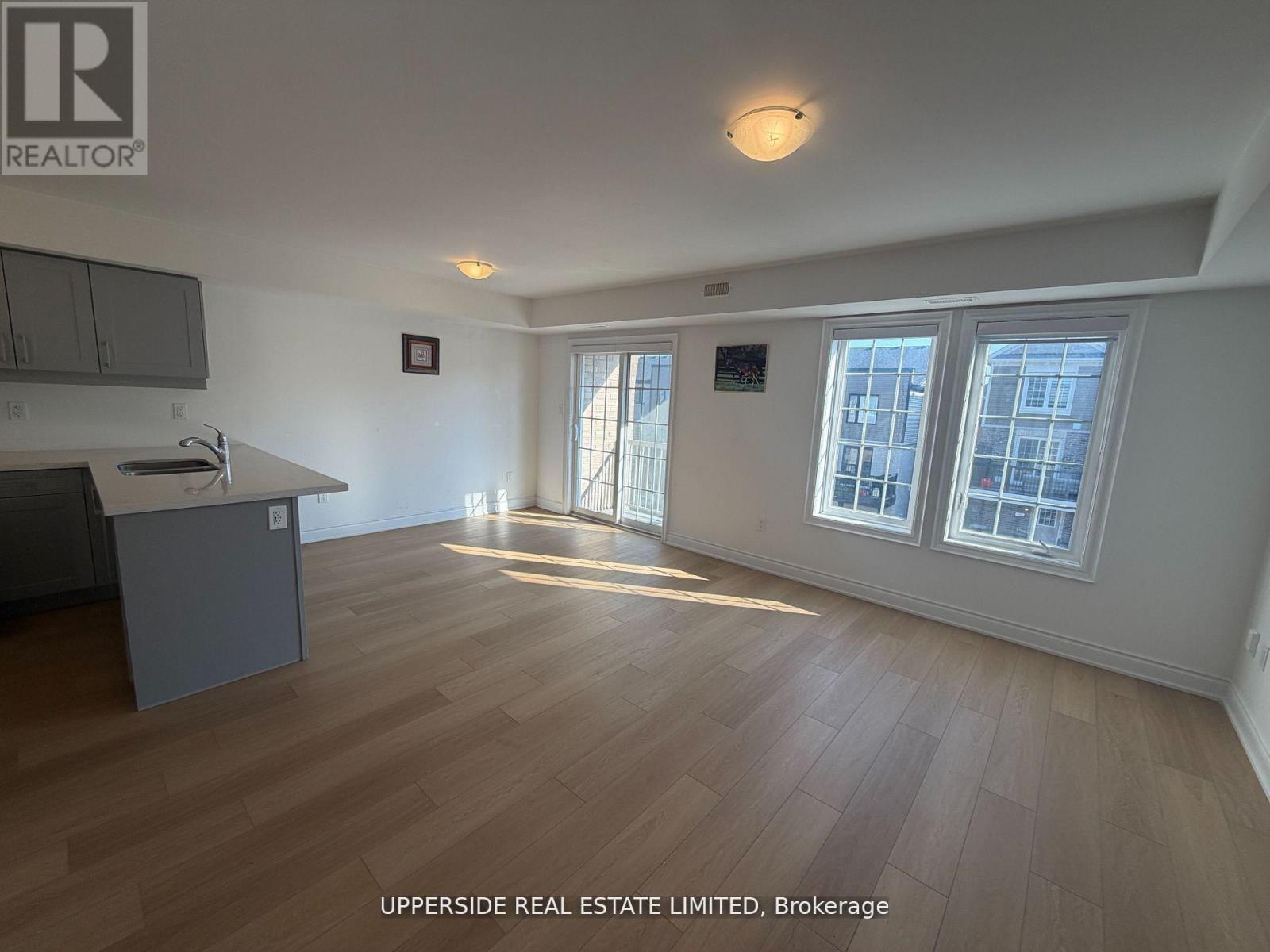 A spacious room with wooden flooring and a kitchen area with a counter and cabinets.