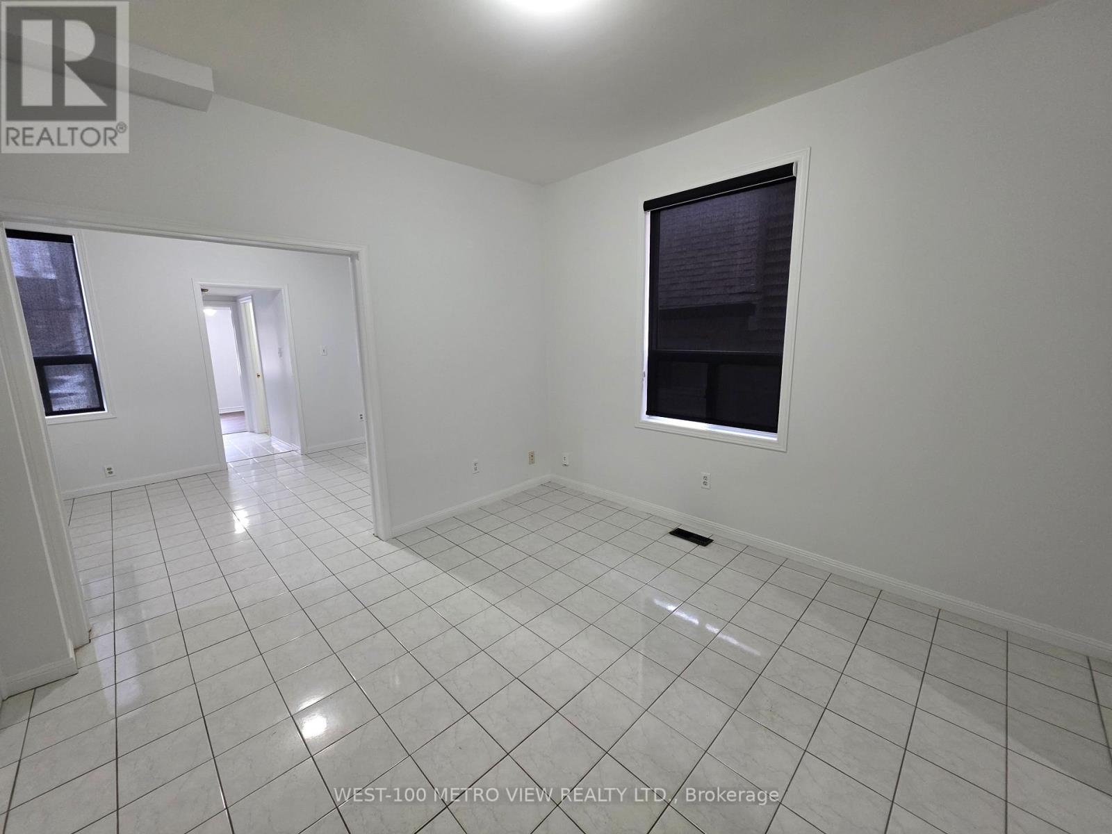 A white tiled room with a window and a door leading to another room.