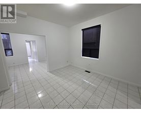 A white tiled room with a window and a door leading to another room.