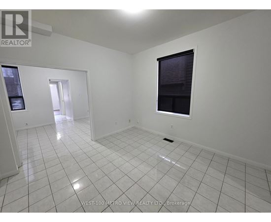 A white tiled room with a window and a door leading to another room.