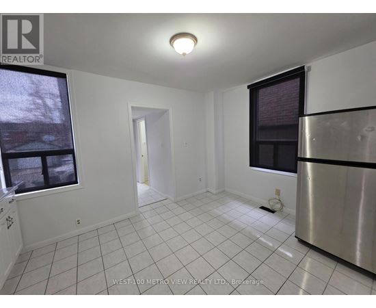 A white tiled kitchen with a stainless steel refrigerator and a window.