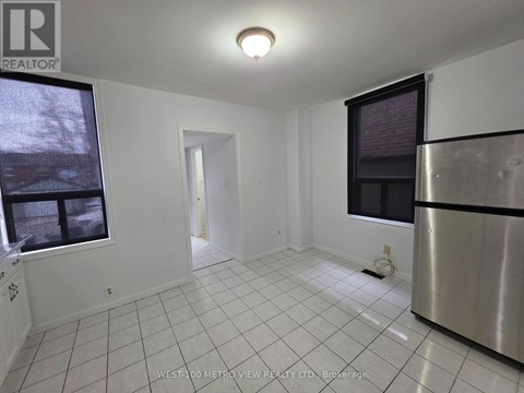 A white tiled kitchen with a stainless steel refrigerator and a window.