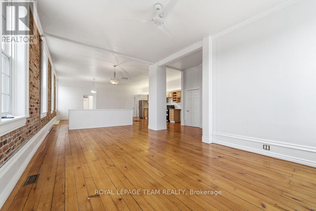 A spacious room with wooden floors and white walls, with a brick wall on the left side.