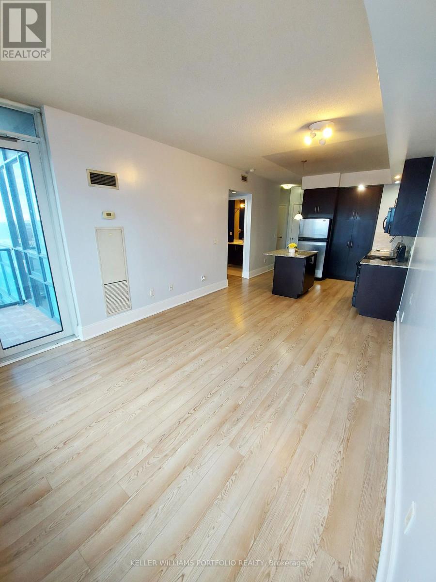 A spacious room with wooden flooring and a large window.
