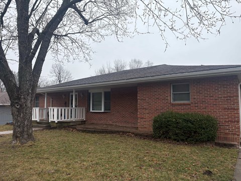 A red brick house with a white porch and a tree in front.