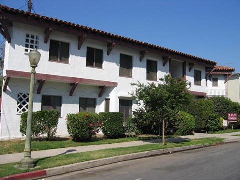 A white building with a red tile roof and a green lamp post in front.