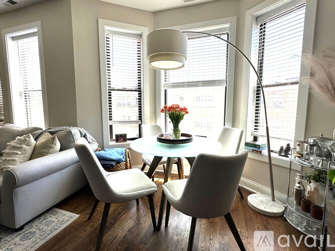 A living room with a white couch, a round table with a vase of flowers, and a floor lamp.