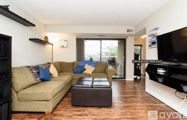 A living room with a beige couch and a brown ottoman.
