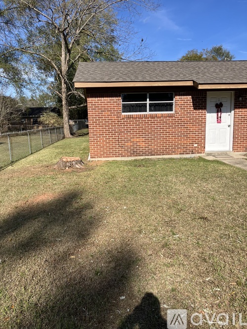A small red brick building with a white door and a white fence in front.