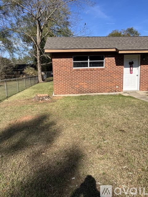 A small red brick building with a white door and a white fence in front.