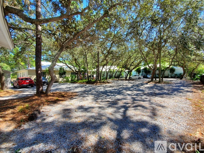 A gravel driveway leads to a house with a red car parked in front.