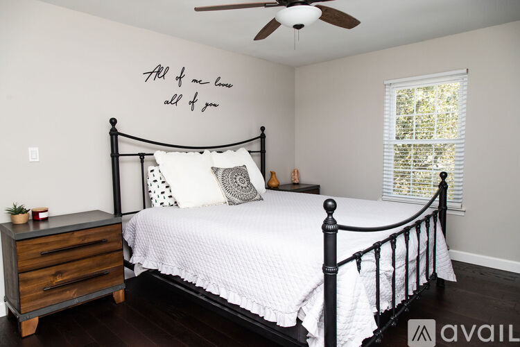 A bedroom with a bed, dresser, and a wall decoration that says "All of me love all of you".
