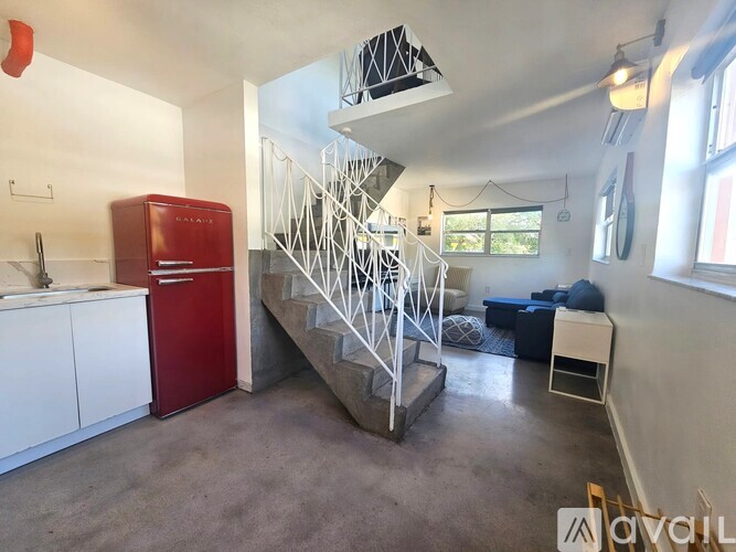 A red fridge sits in a kitchen with a staircase in the middle of the room.