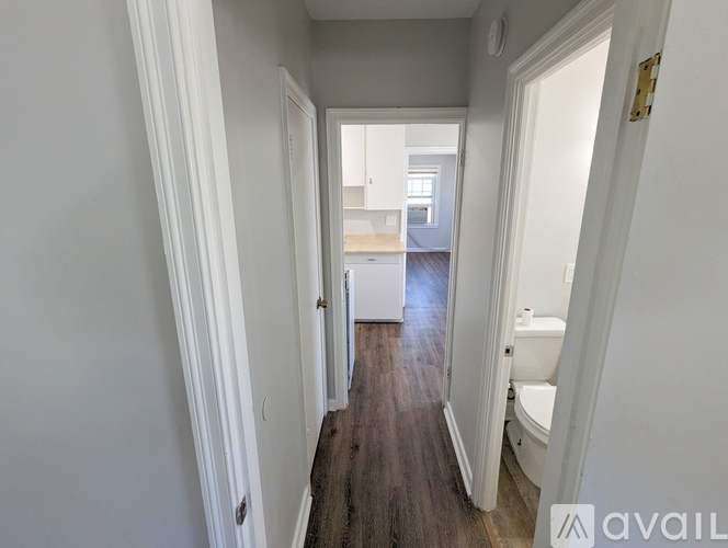 A hallway with a wooden floor leads to a bathroom.