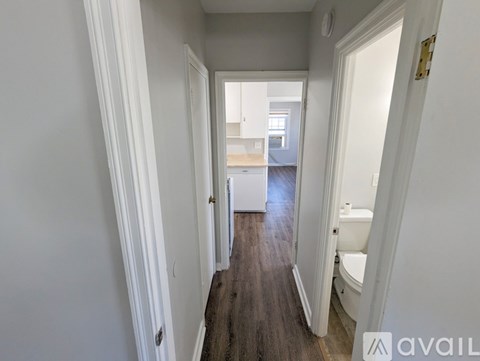 A hallway with a wooden floor leads to a bathroom.