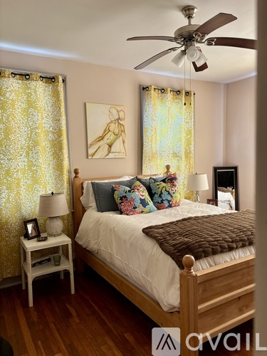 A bedroom with a bed, a ceiling fan, and a painting on the wall.