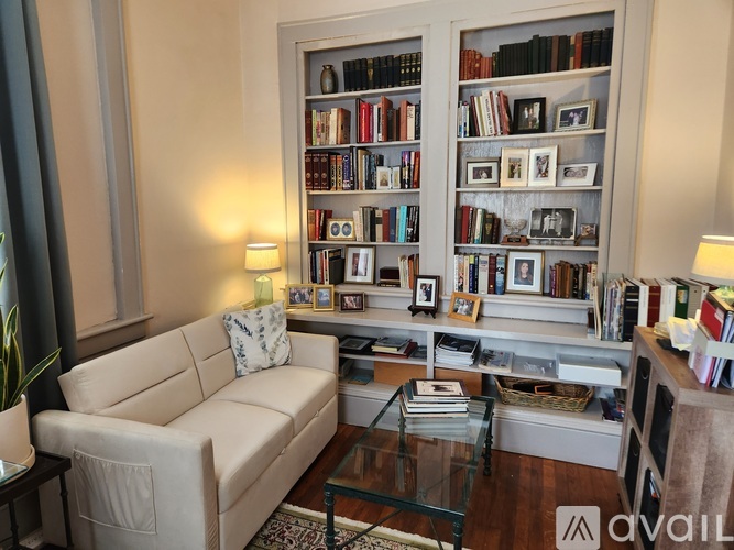 A living room with a white couch, a glass coffee table, and a bookshelf filled with books and picture frames.