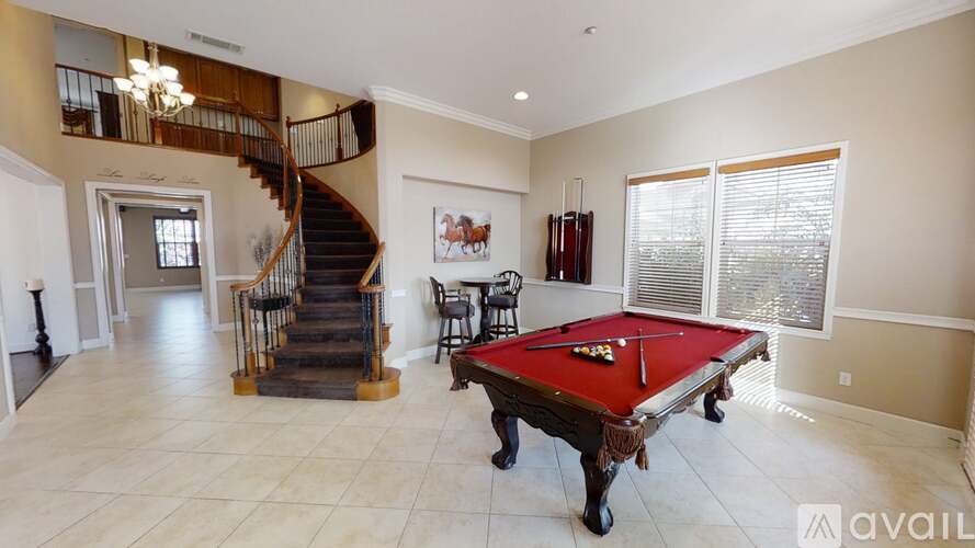 A pool table is in the middle of a spacious room with a staircase.